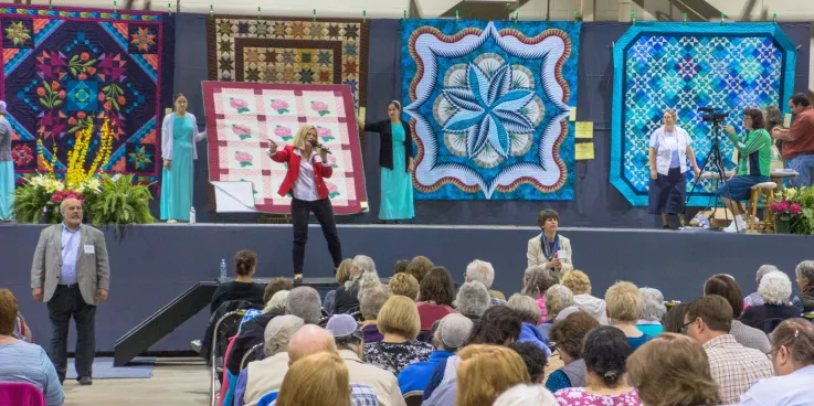  People sitting in audience for quilt auction.