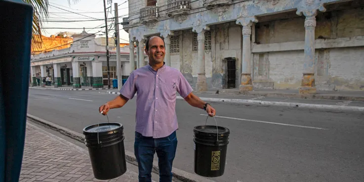 A man from Cuba holds two relief kits on a sidewalk. 