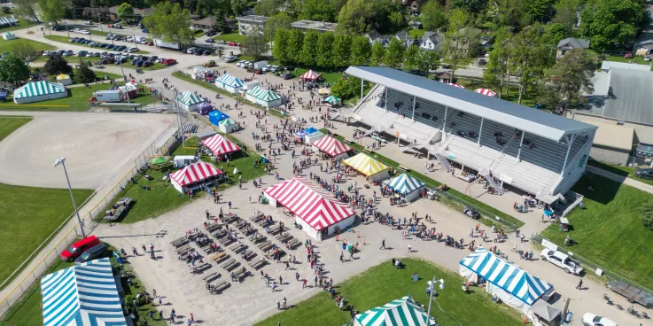 A photo from several feet in the air which shows several tents, a grandstand, and visitors on the ground.