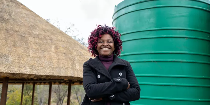 Woman stands beside water tank, smiling.