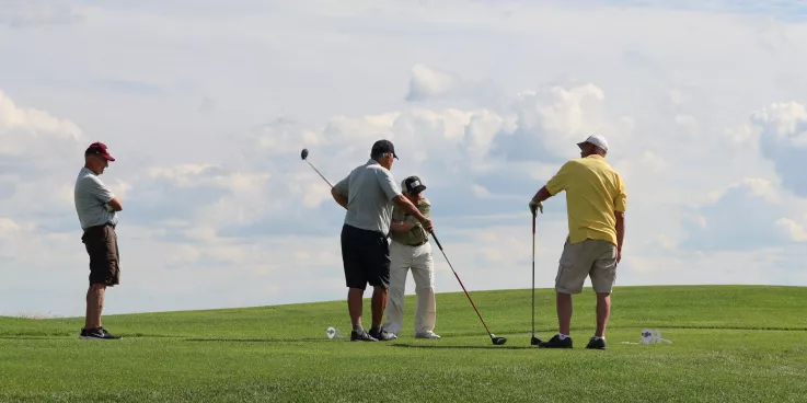 four golfers on a green in front of a blue sky