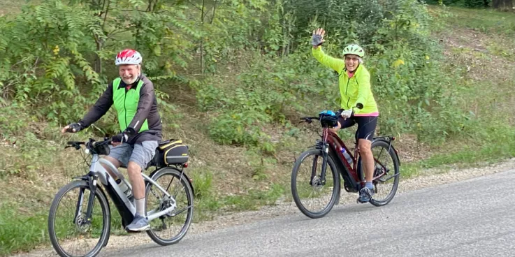 two people riding bicycles wave to the camera