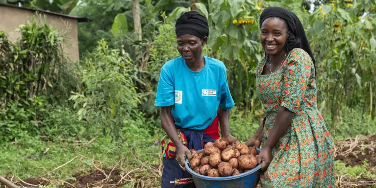 Two women carrying potatoes on a farm.