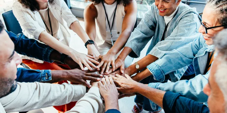 Individuals of varying age and race form a circle with their hands coming together in the centre.