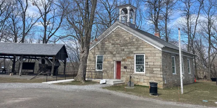 A grey brick building with a bell tower next to a smaller pavilion type structure. 