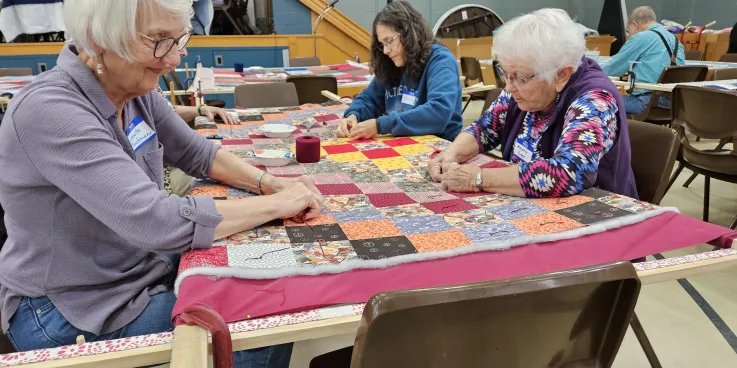 A group of people knot a comforter.