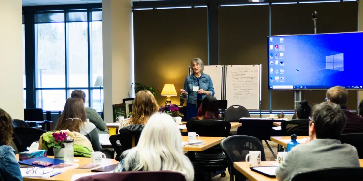 A woman presents to a group of people at the front of a room.