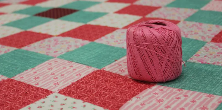 multi color square comforter and a pink ball of yarn sitting on top.