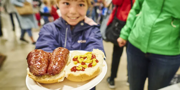 A girl holding a plate of farmers sausage on a bun