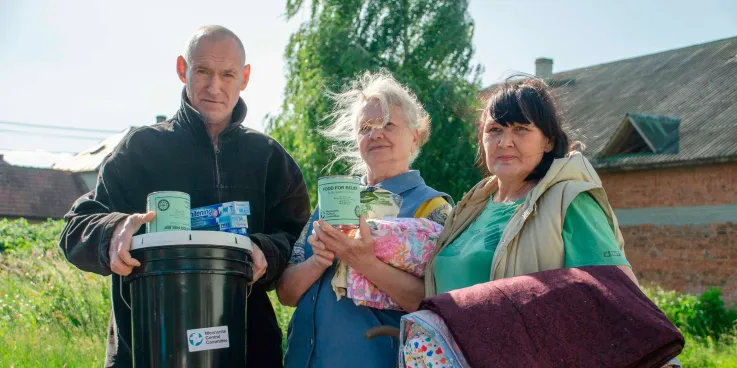 A man and two women hold up relief kit items and quilts