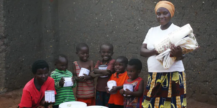 Nizigama Bestide, who lives in Dzaleka Refugee Camp in Malawi, stands with her children Ngurunziza Neema, Venist Neema, Press Neema, Gard Neema, Erie Neema, and Kabura Oneszima. The family is holdin