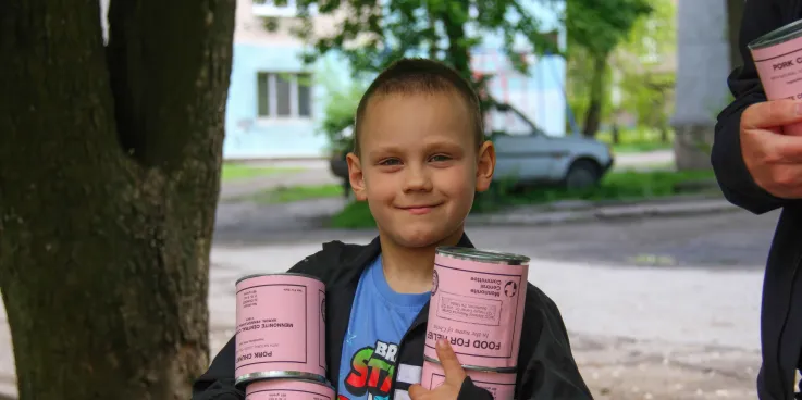A boy* holds cans of meat he and his mother (not pictured) received from volunteers with MCC partner Association of Mennonite Brethren Churches of Ukraine (AMBCU). The canned meat was part of a distri