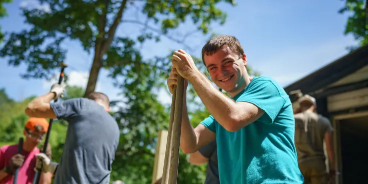 Micah Dodson, left, Appalachia Build staff, digs a hole for a post to support a wheelchair ramp in Kimball, West Virginia.