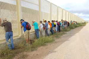 A group of people praying against a border wall