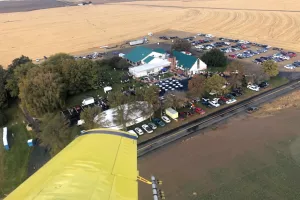 An overview view of a church building during an event. There are a lot of cars parked around the church. The photo was taken out the window of a yellow airplane.