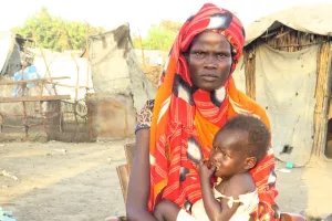 A woman holding a baby in front of a camp for internally displaced people.