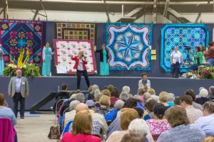  People sitting in audience for quilt auction.