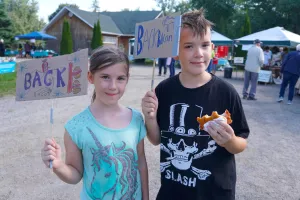 A boy and a girl hold up hand made cardboard signs that read Back Bacon, while the boy eats bacon on a bun.