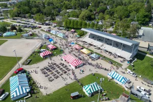 A photo from several feet in the air which shows several tents, a grandstand, and visitors on the ground.