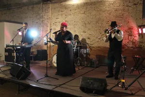 three people performing music playing keyboard, singing, trumpet