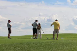 four golfers on a green in front of a blue sky