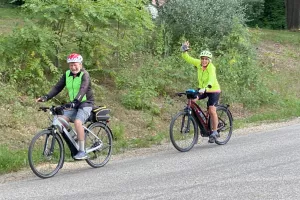 two people riding bicycles wave to the camera