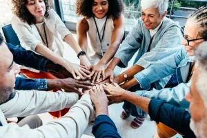 Individuals of varying age and race form a circle with their hands coming together in the centre.