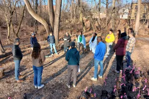 Young adults stand in circle in wooded area.