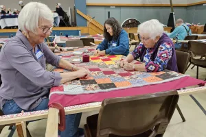 A group of people knot a comforter.