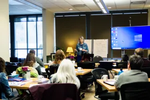A woman presents to a group of people at the front of a room.