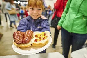 A girl holding a plate of farmers sausage on a bun