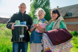 A man and two women hold up relief kit items and quilts