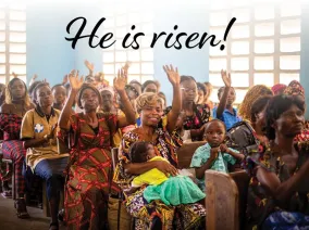 People in a church with hands raised and the words "He is risen!"