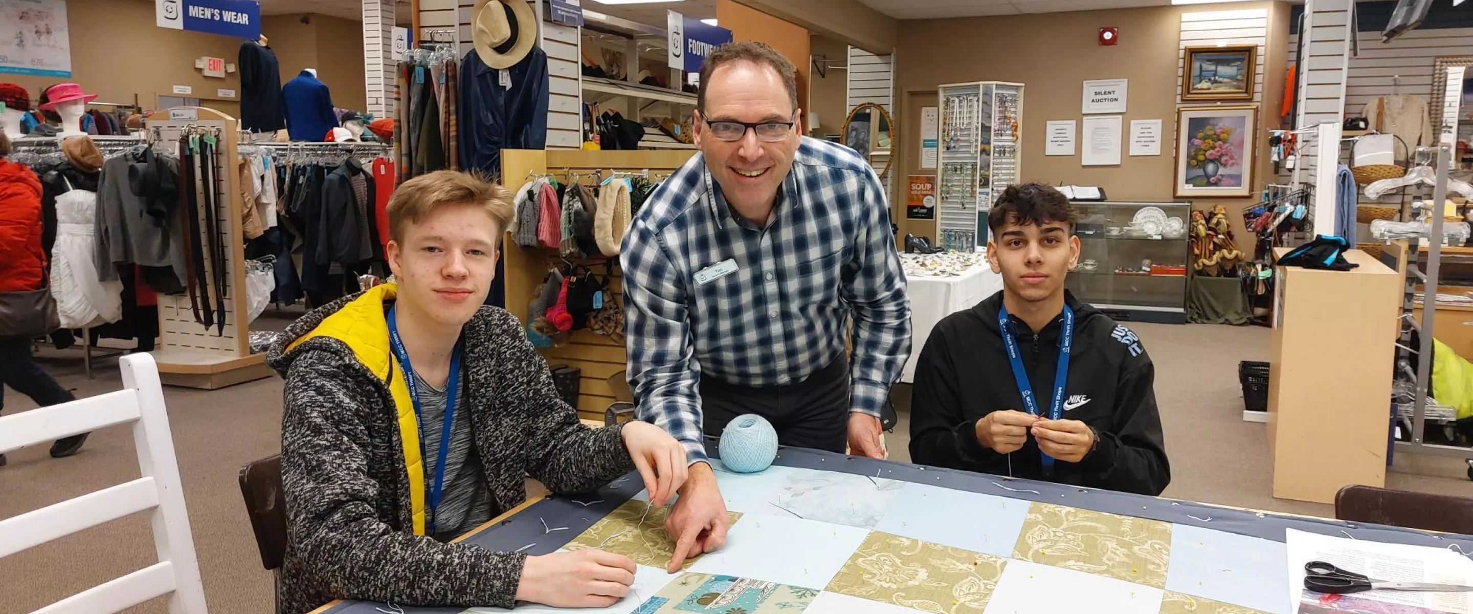 Two youth and an adult pose for the camera while sitting around a comforter in a thrift shop.