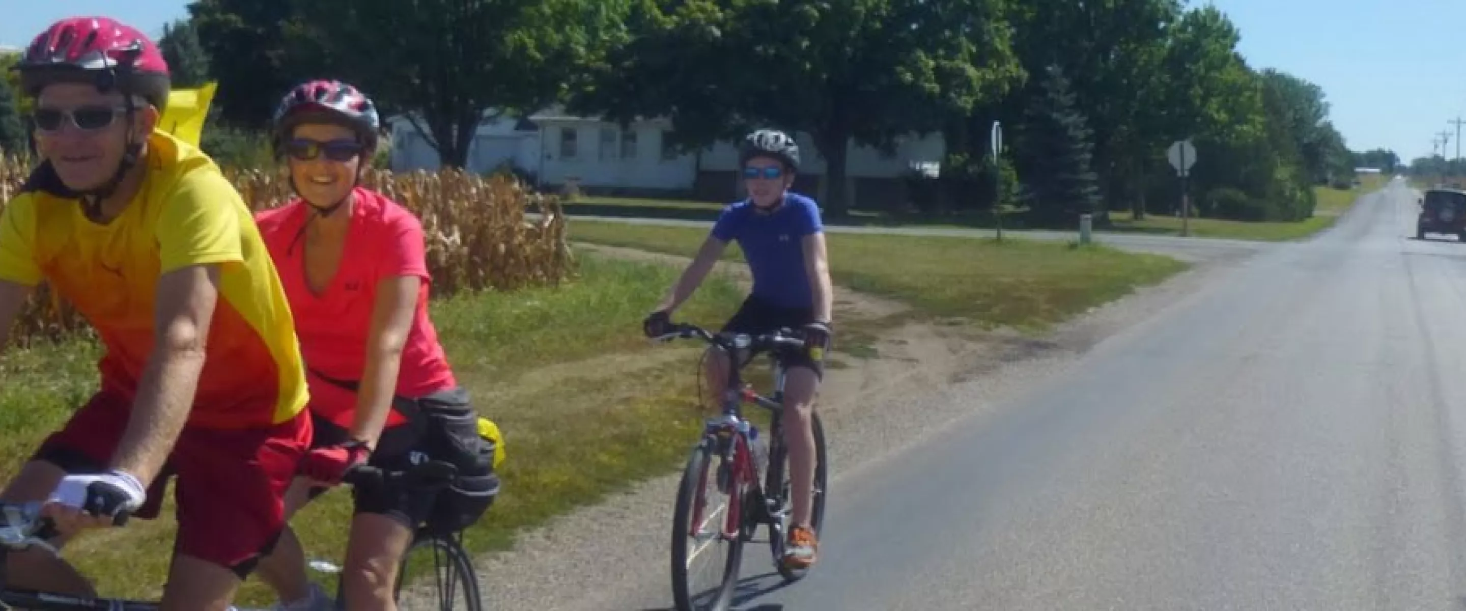 Two people ride a tandem bike while another cyclist follows behind them.