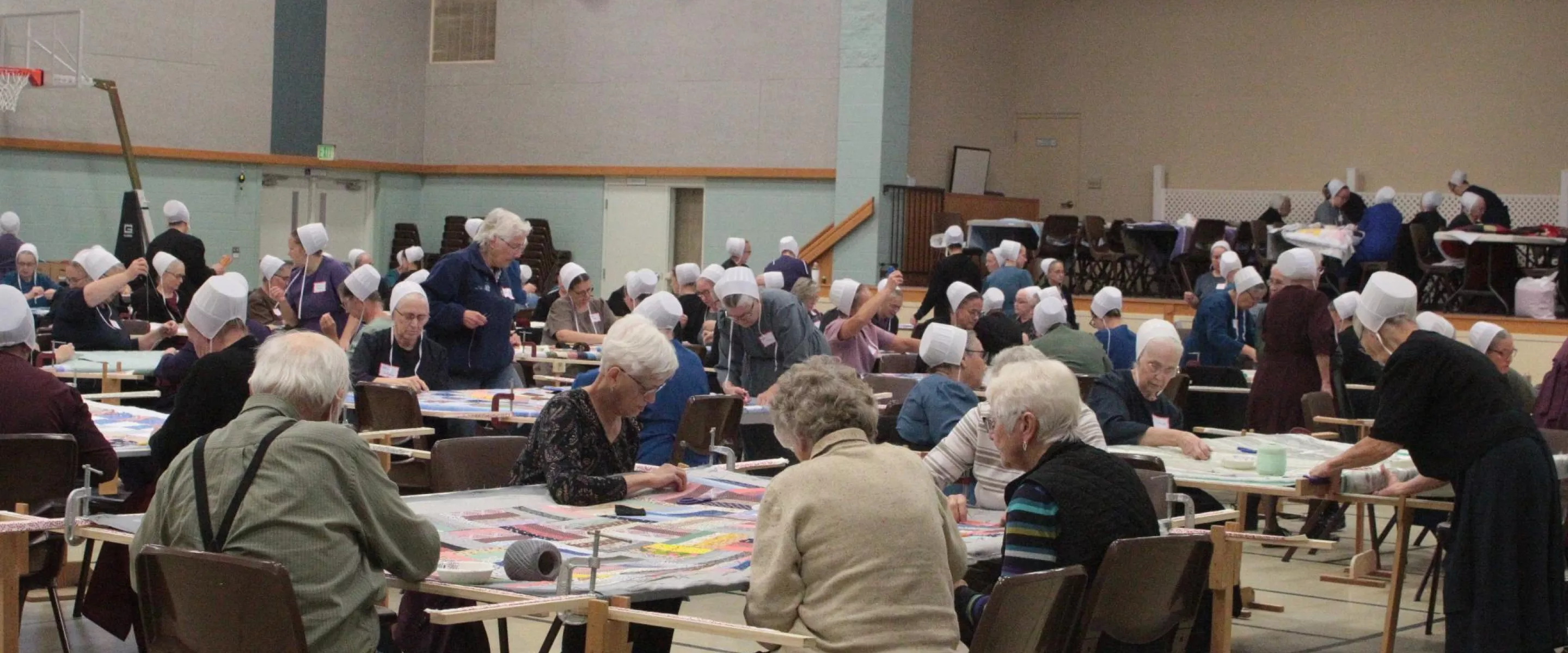 A large group of people sit around comforter tops and tie them.