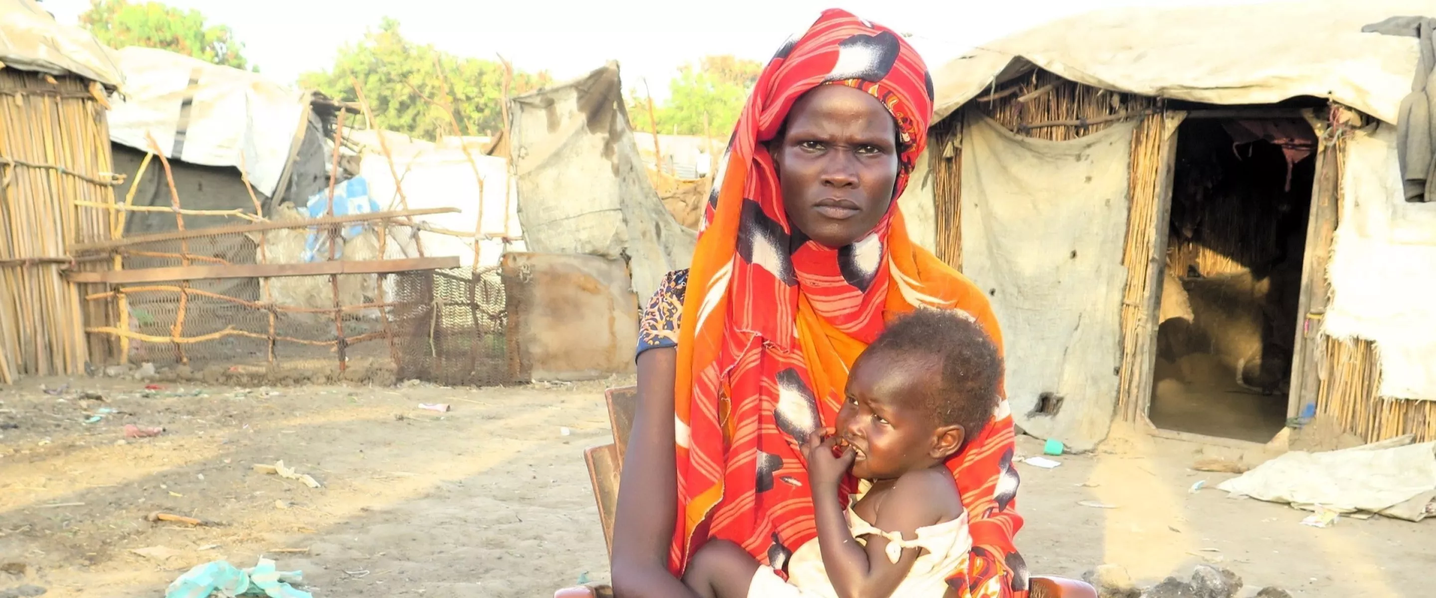 A woman holding a baby in front of a camp for internally displaced people.