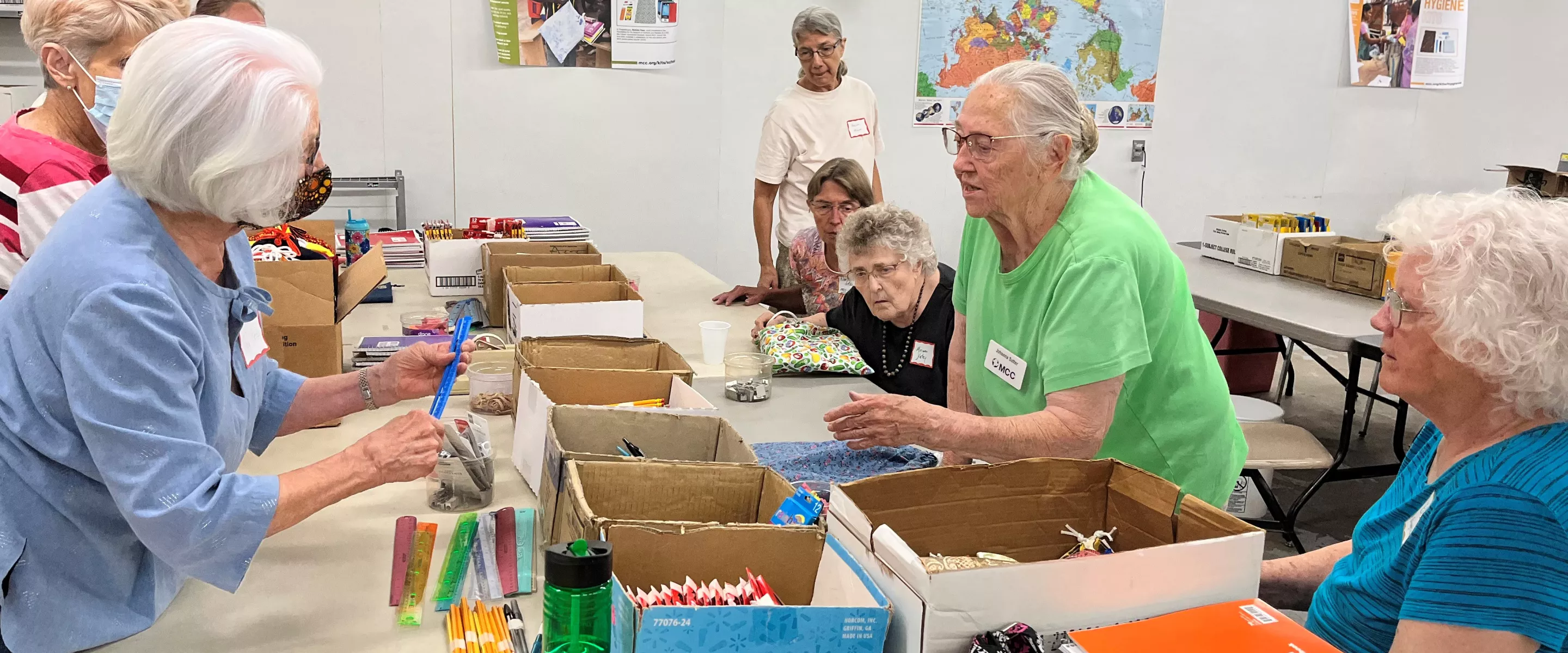 women stand around table putting together school kits