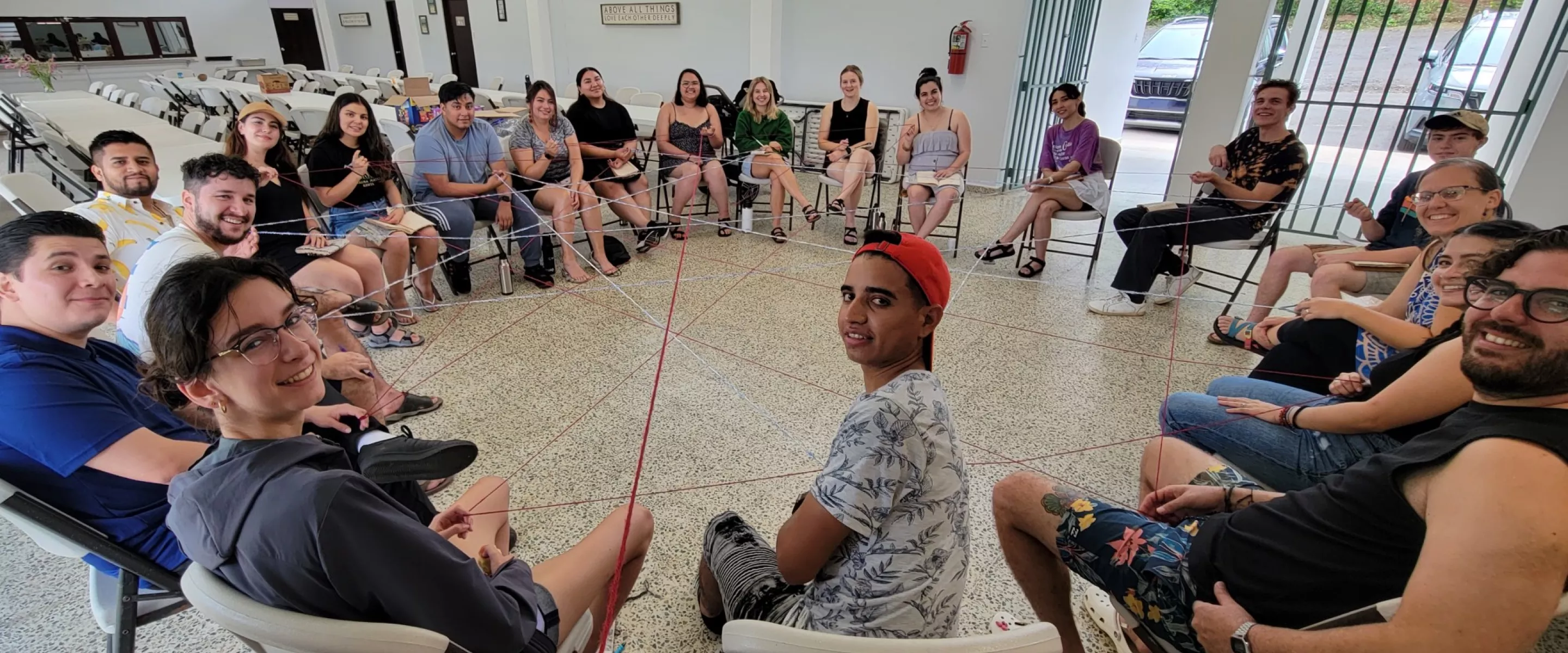 Young people sitting in a circle connected by web of string.