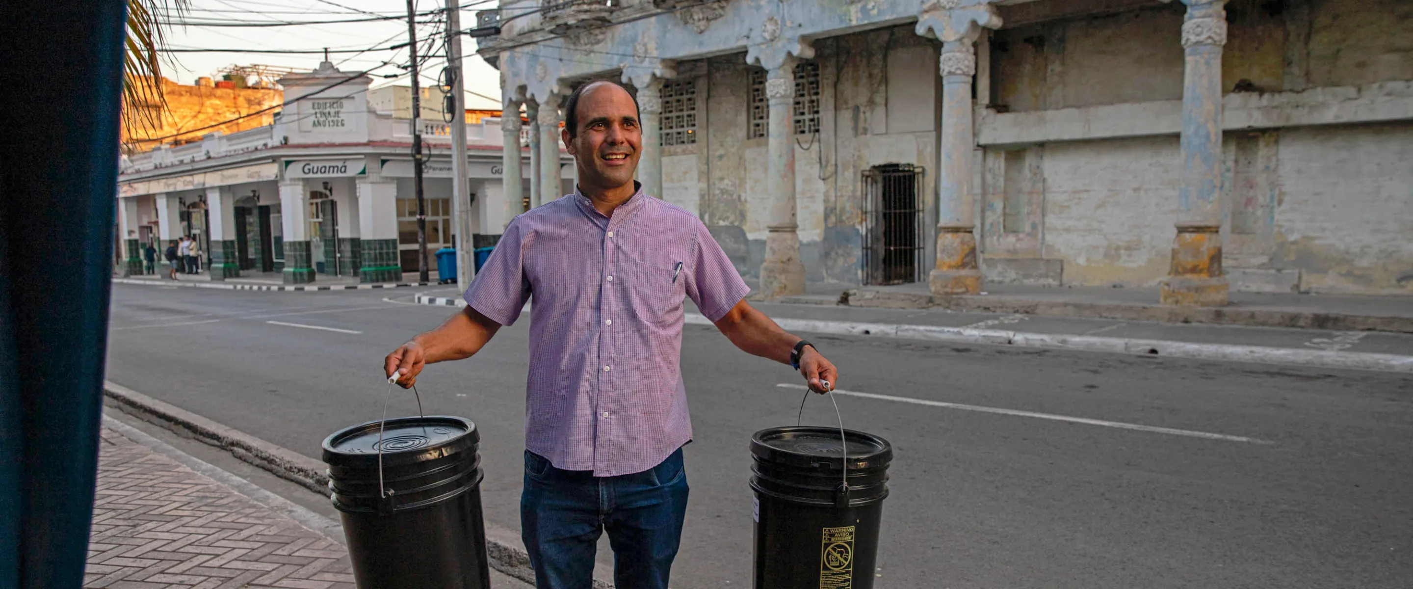 A man from Cuba holds two relief kits on a sidewalk. 