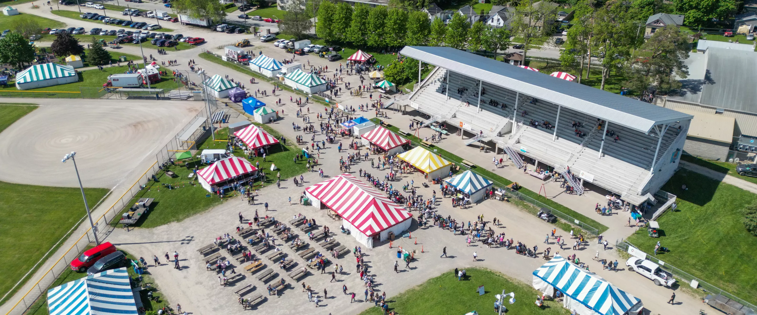 A photo from several feet in the air which shows several tents, a grandstand, and visitors on the ground.