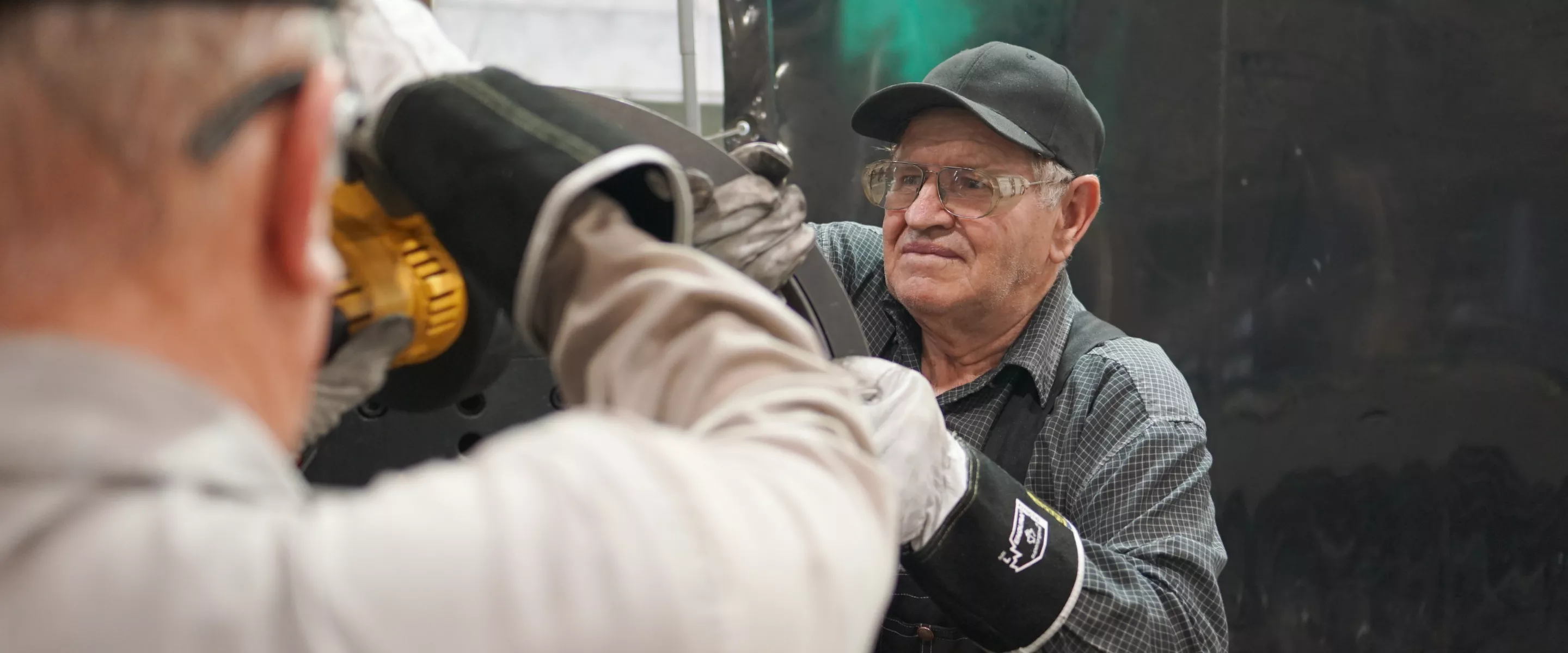 Two men lift a heavy object. The man facing the camera is wearing a black hat and dark clothes.