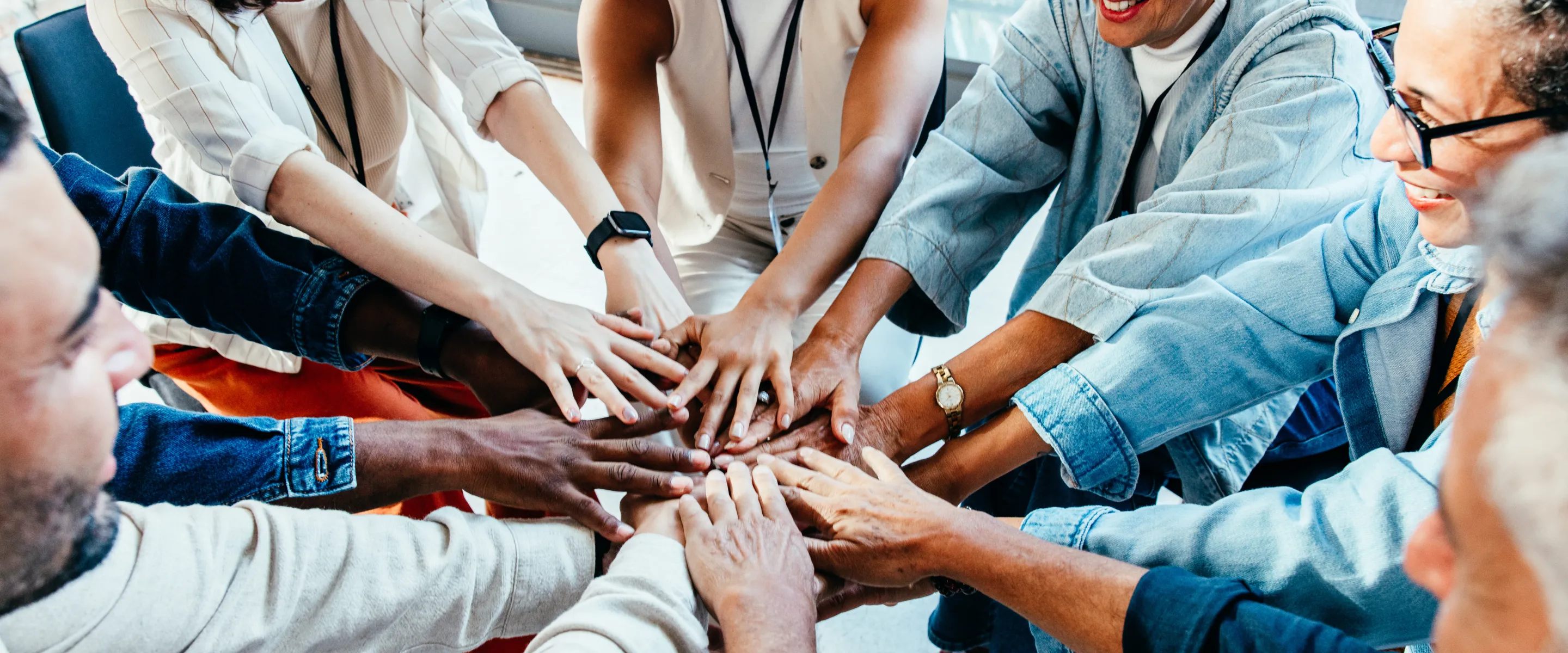 Individuals of varying age and race form a circle with their hands coming together in the centre.