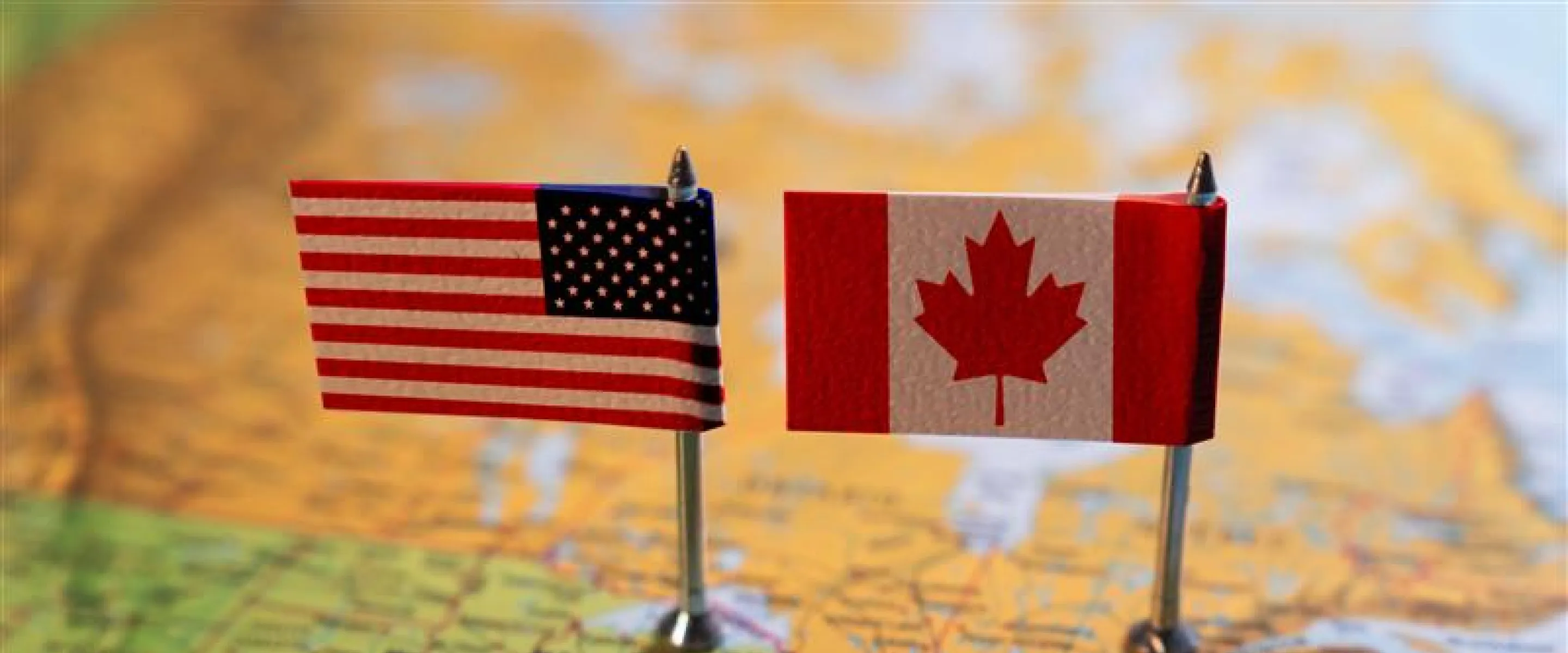 An American flag and Canadian flag next to one another while sitting on top of a map.