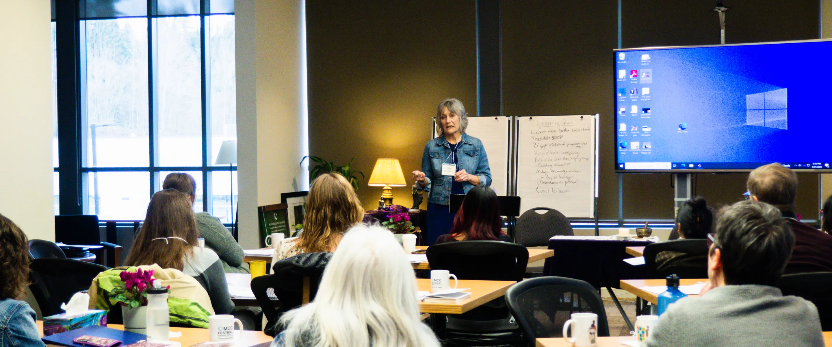 A woman presents to a group of people at the front of a room.