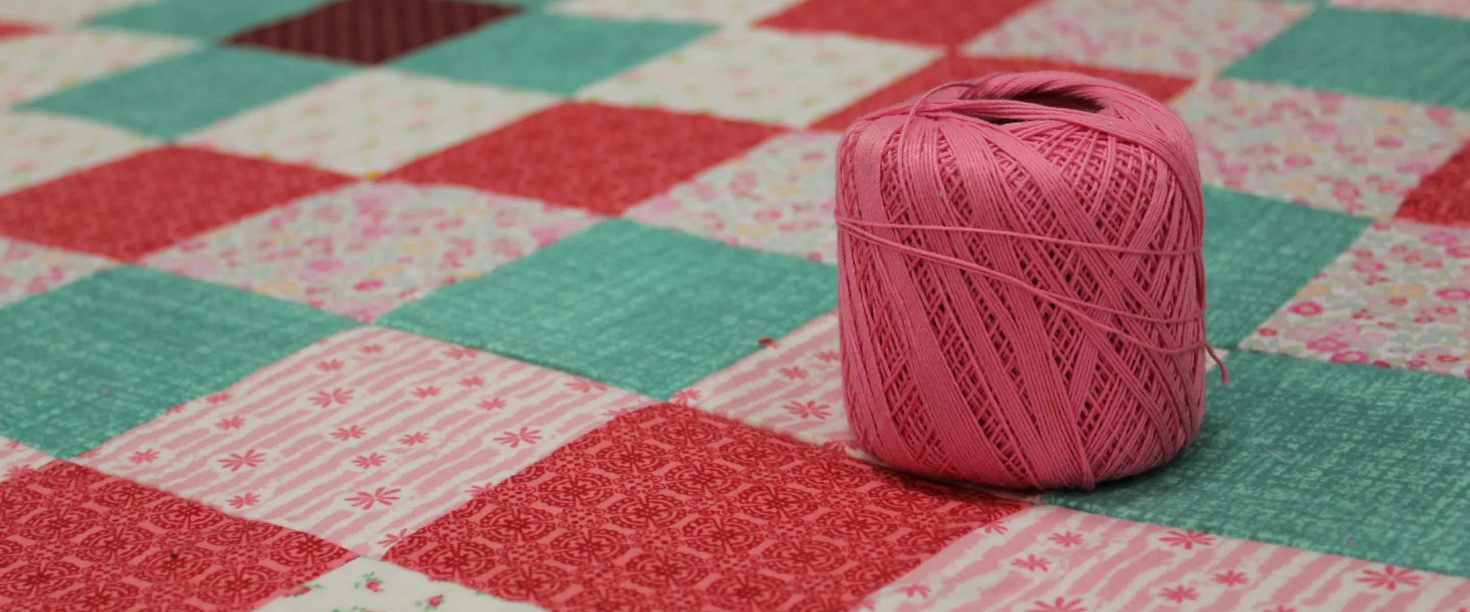 multi color square comforter and a pink ball of yarn sitting on top.