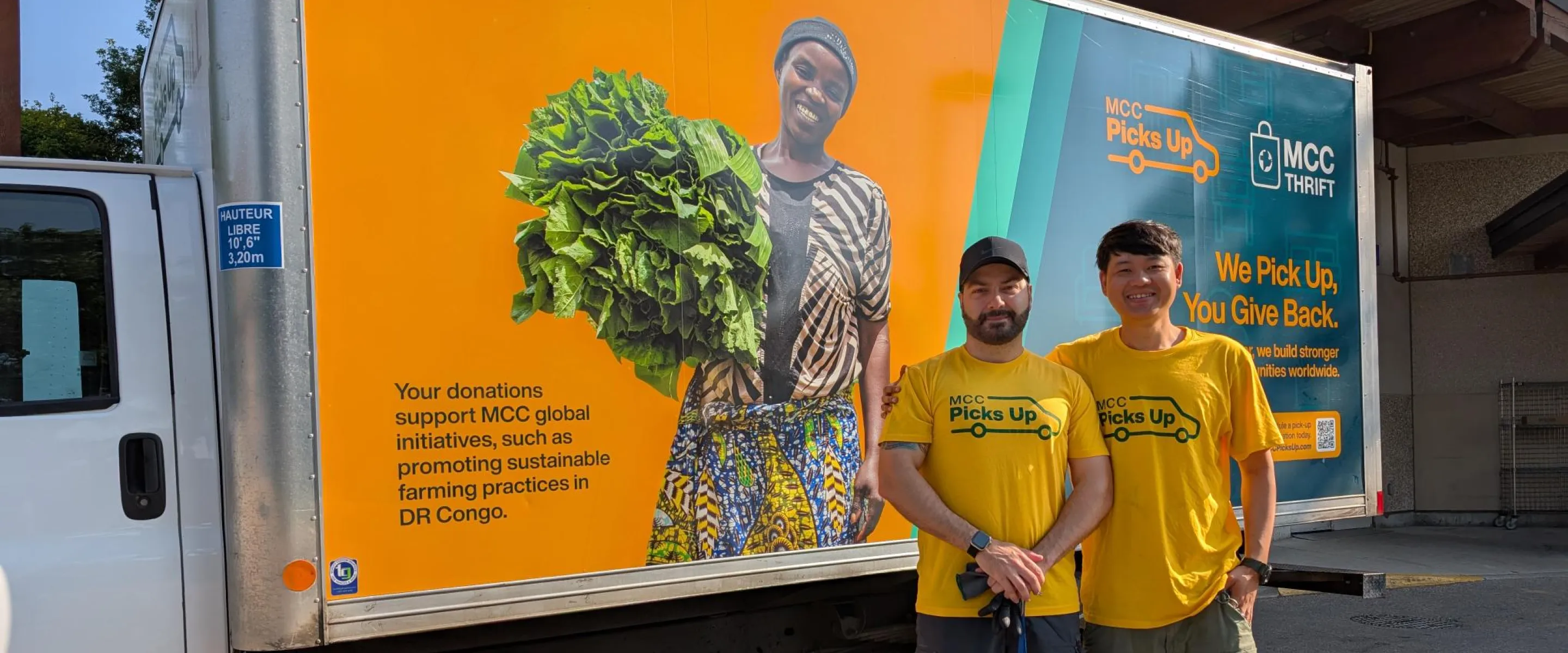 Two men in yellow stand in front of an MCC Thrift truck that is also yellow with images on it.