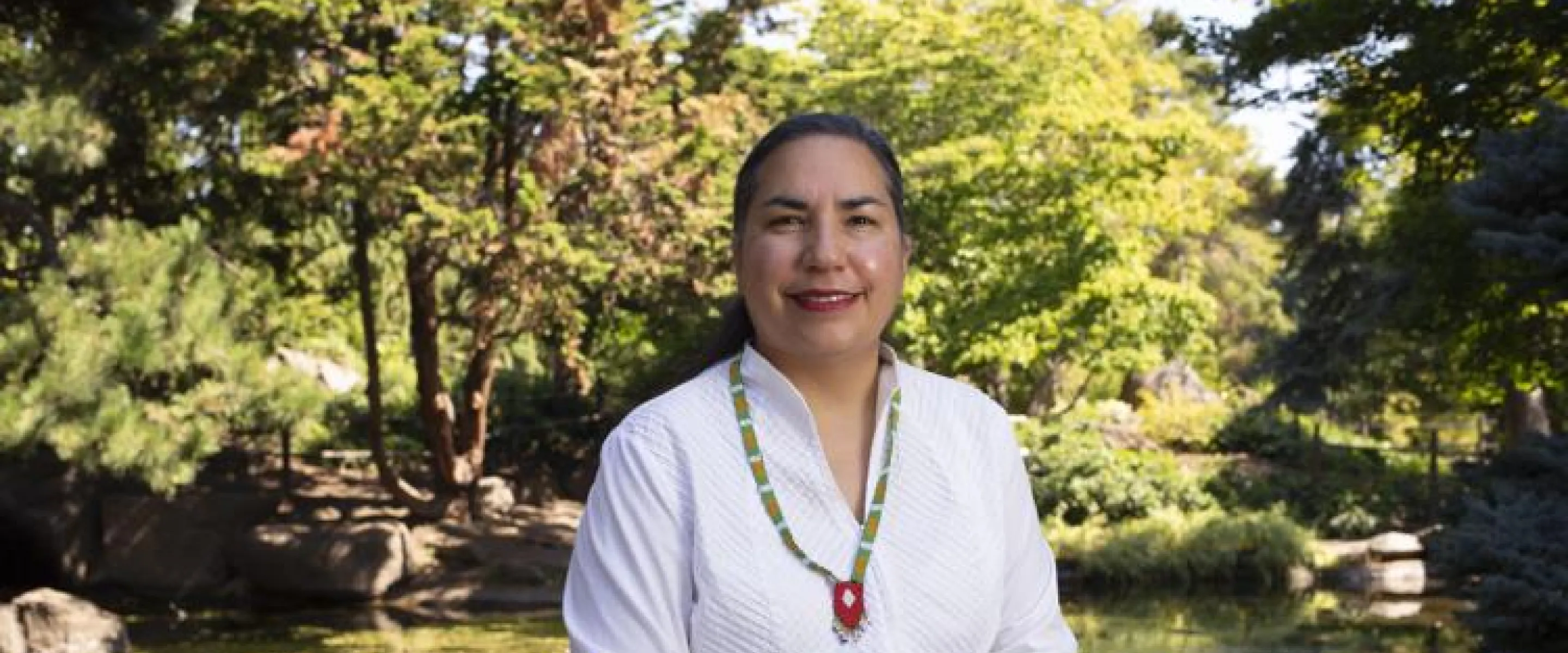 A woman wearing a white shirt sits in front of a lush green landscape.