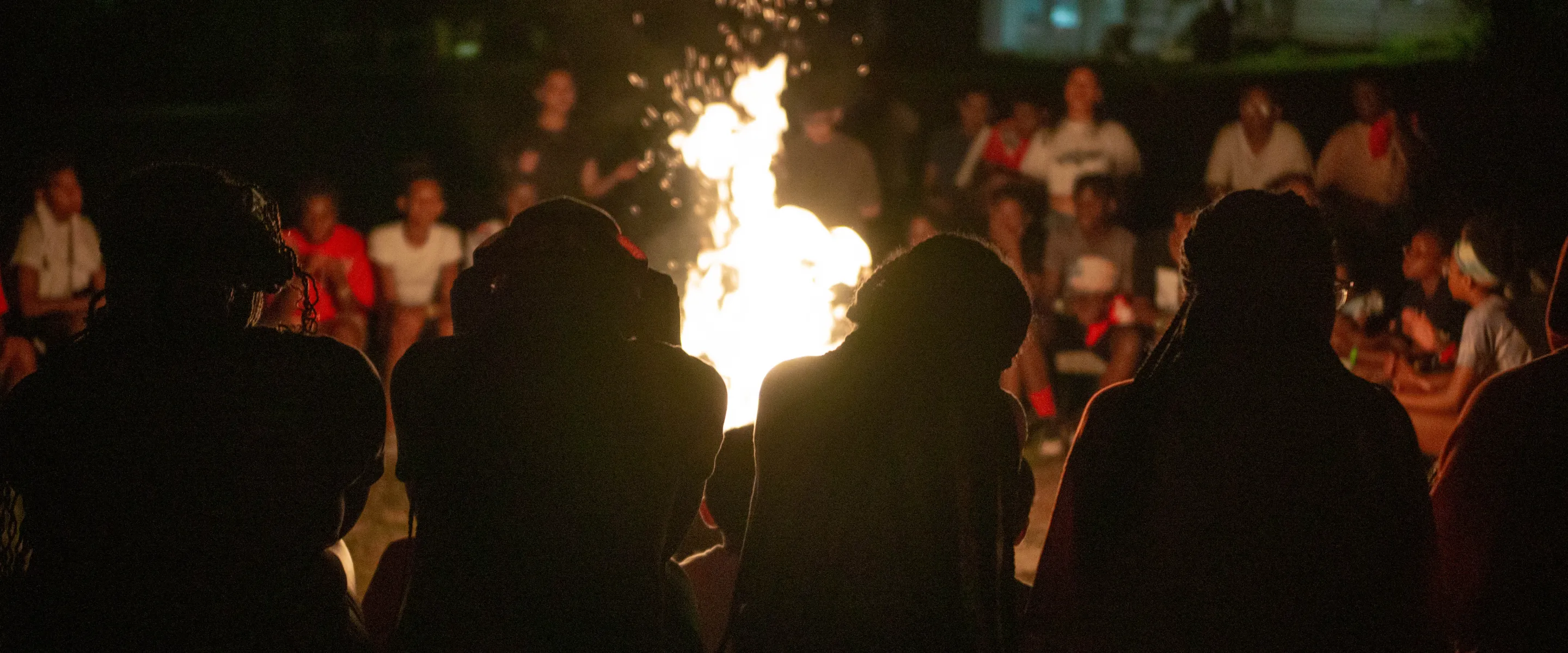 Four youth sit in front of campfire