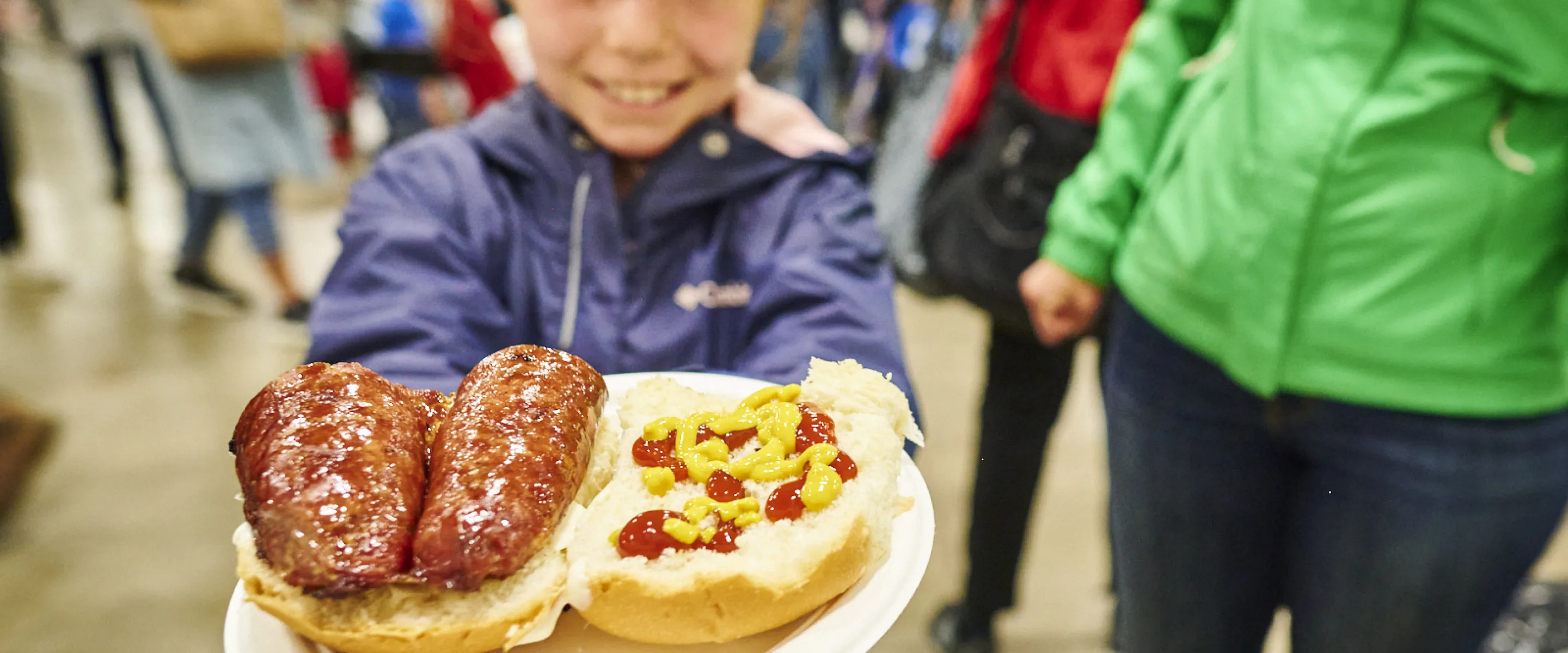 A girl holding a plate of farmers sausage on a bun